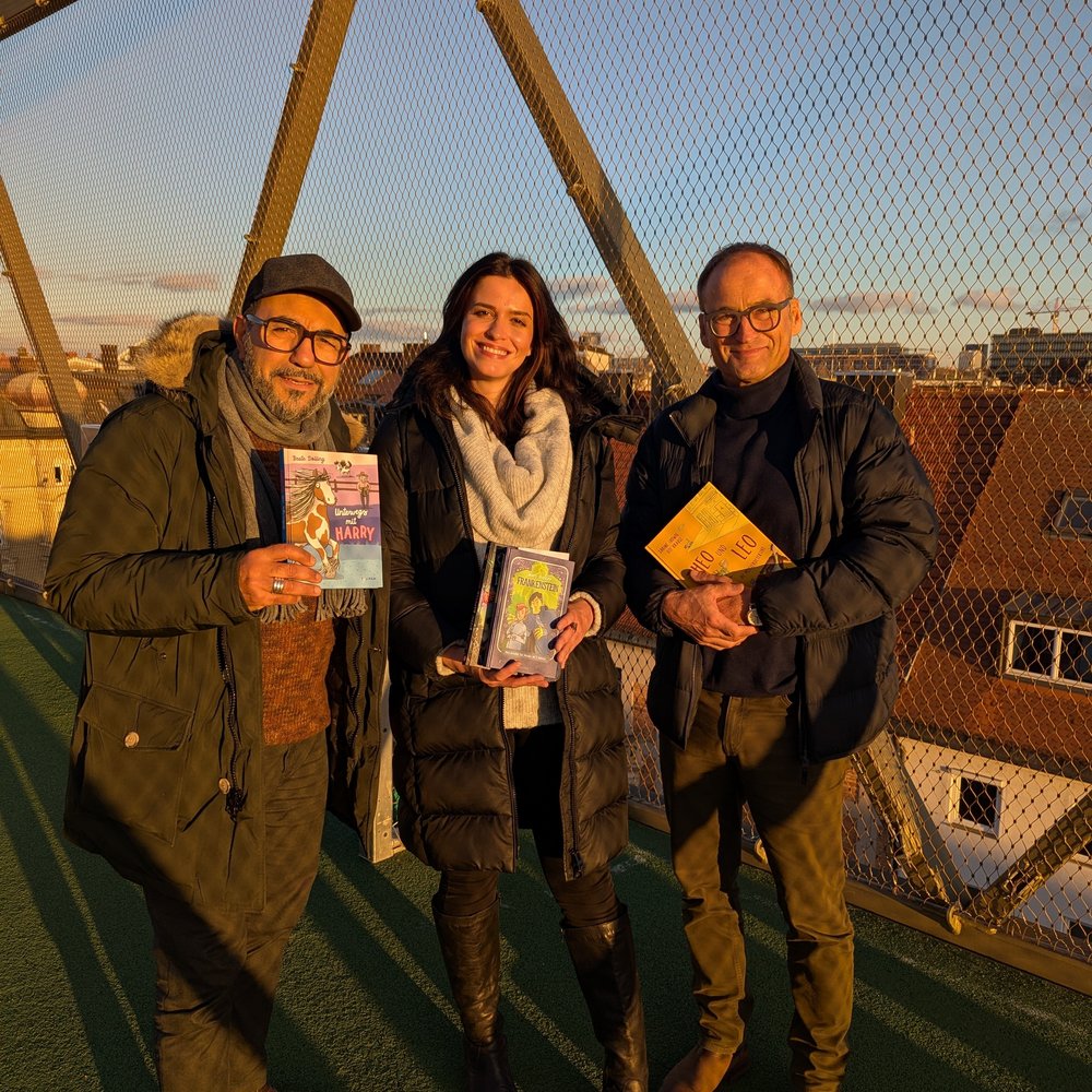 Thomas Rathnow, Vorstandsvorsitzender der Stiftung Lesen, Lesebotschafter Adnan Maral und Autorin Yasmin Shakarami stehen auf einer Brücke und zeigen die von ihnen vorgelesenen Bücher.